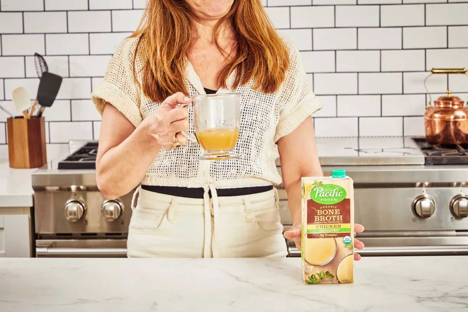 A person holds a glass of Pacific Foods Chicken Bone Broth