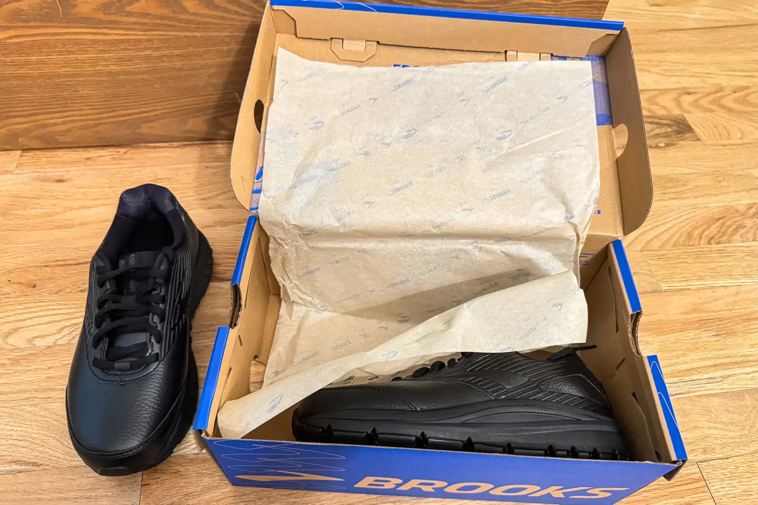 A pair of Women's Addiction Walker 2 Sneakers with one shoe out of the box and the other inside on a wooden floor