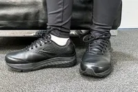 A person wearing Women's Addiction Walker 2 Sneakers and leggings near on a bench