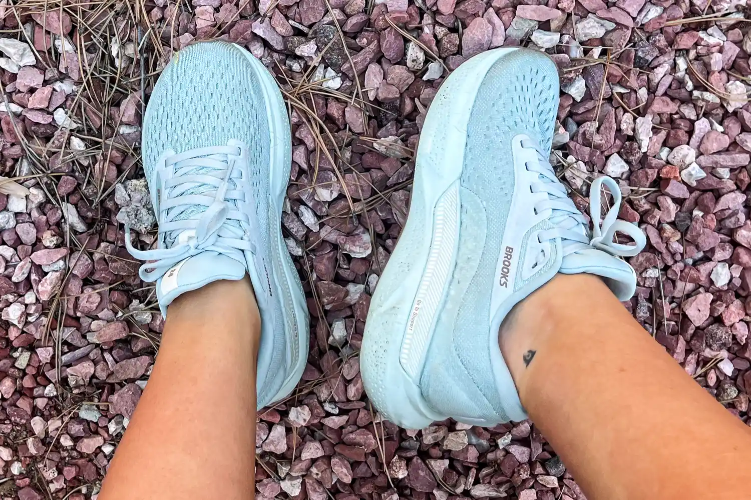 A pair of athletic shoes is shown worn on feet over rocky ground