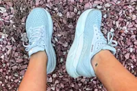 A pair of athletic shoes is shown worn on feet over rocky ground