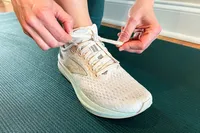A person tying the laces of a running shoe labeled 'Brooks' on a yoga mat