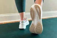 Close-up of a person wearing athletic shoes stepping onto a yoga mat