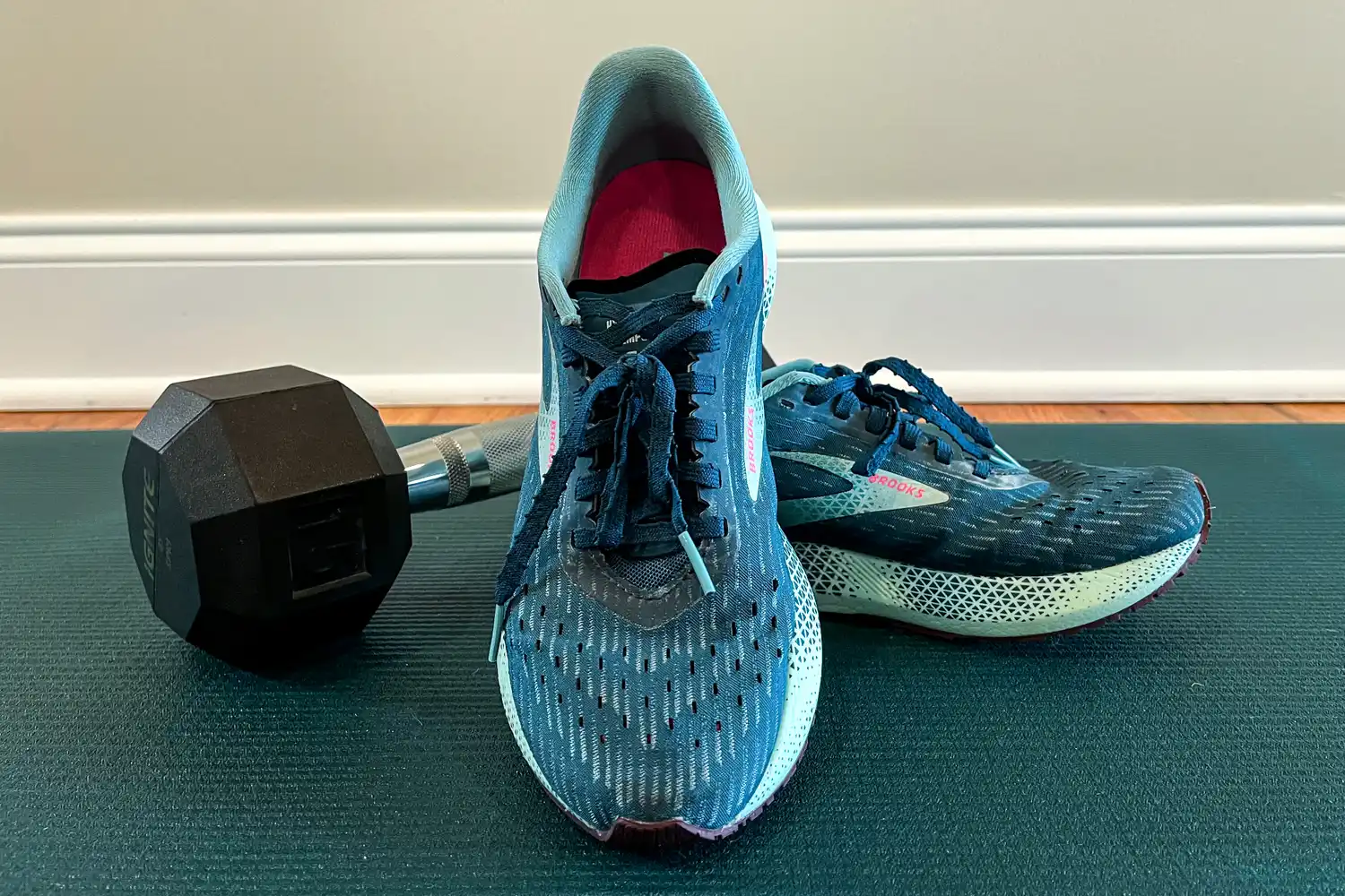 A pair of running shoes and a dumbbell on a yoga mat indoors