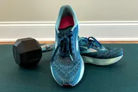 A pair of running shoes and a dumbbell on a yoga mat indoors