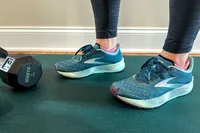Person wearing athletic shoes standing on a mat near a dumbbell