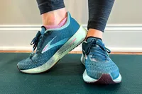 Close-up of someone's feet wearing running shoes on a yoga mat, showing the design and fit of the footwear
