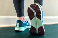 Close-up of a person walking wearing running shoes on a mat, showing the sole of one shoe