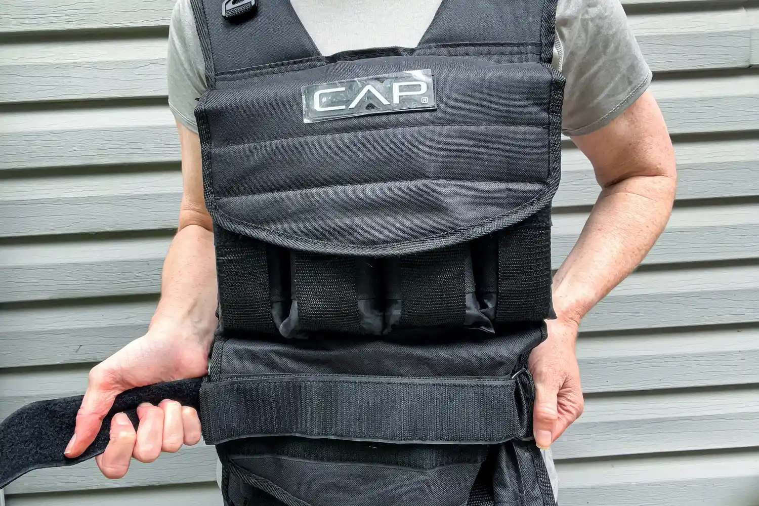 A person secures the waist strap on the CAP Barbell 20-150 Lb Adjustable Weighted Vest