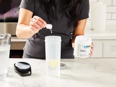 A person pours a scoop into Klean Athlete Klean Creatine