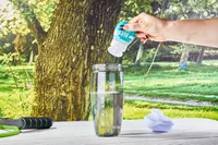 A hand adding Buoy Electrolyte Drops to a glass of water on a table outside