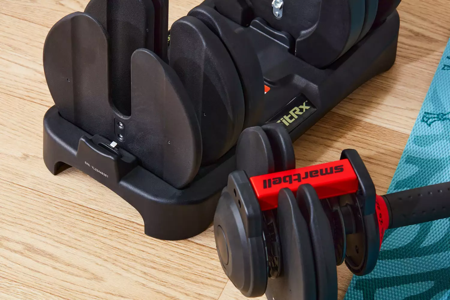 FitRx SmartBells Set Quick Select Adjustable Dumbbells next to its stand on wood floor