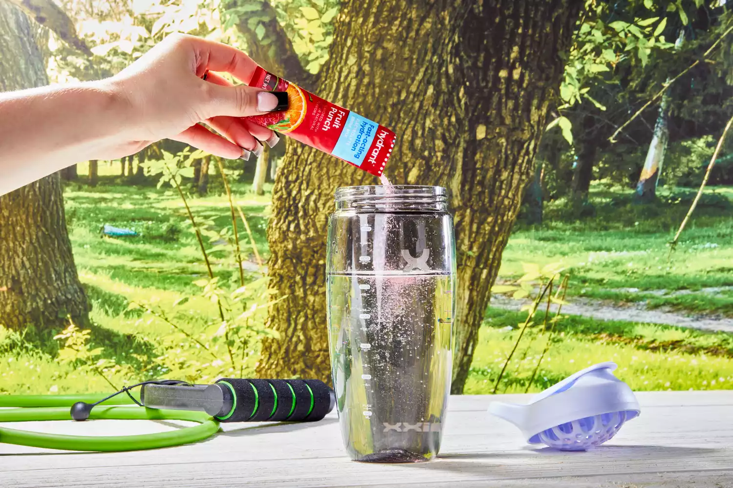 A hand adding Hydrant Hydrate Hydration Drink Mix to a glass of water outdoors
