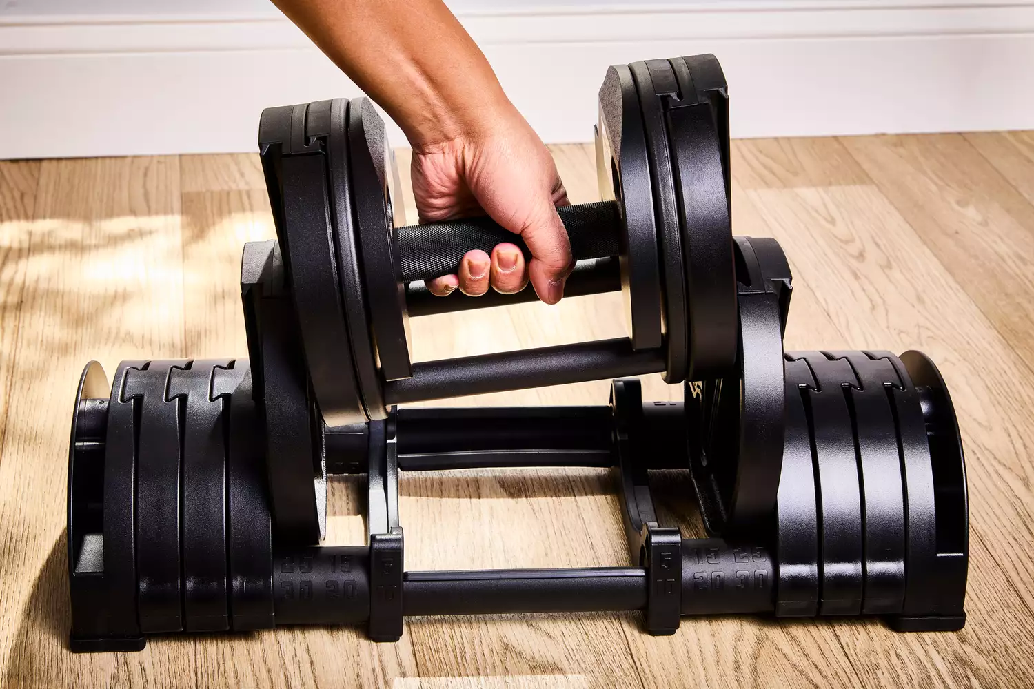 A person places the Rep Fitness Quickdraw Adjustable Dumbbell back into its base