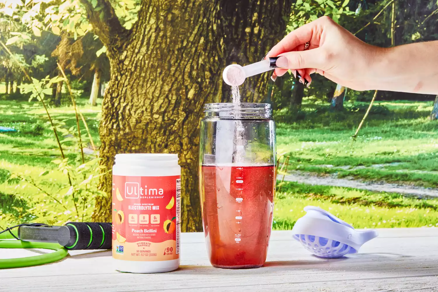 A scoop adding Ultima Replenisher Electrolyte Hydration Powder into a glass of water