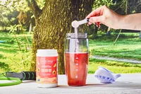 A scoop adding Ultima Replenisher Electrolyte Hydration Powder into a glass of water