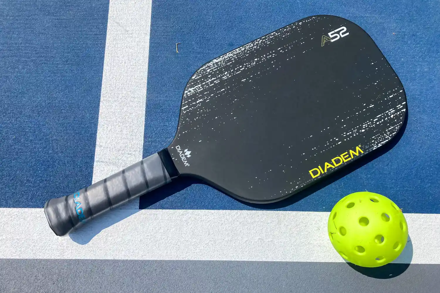 The Diadem A52 Pickleball Paddle next to a pickleball
