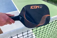 A person rests the Diadem Icon Infinity Pro Pickleball Paddle on a pickleball net