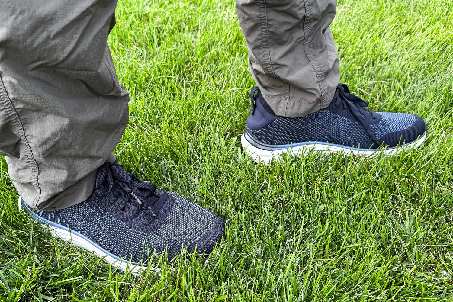 A person wearing pants and Dr. Scholl's Men's Feel Ready Lace Up Sneakers standing on grass