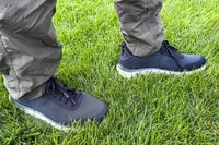 A person wearing pants and Dr. Scholl's Men's Feel Ready Lace Up Sneakers standing on grass