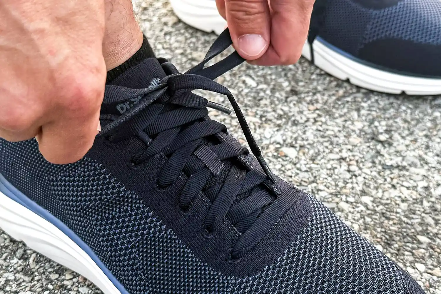 A person tying shoelaces on a pair of Dr. Scholl's Men's Feel Ready Lace Up Sneakers