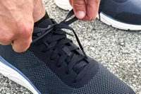 A person tying shoelaces on a pair of Dr. Scholl's Men's Feel Ready Lace Up Sneakers