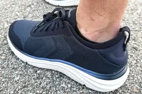 A foot wearing the Dr. Scholl's Men's Feel Ready Lace Up Sneakers on asphalt