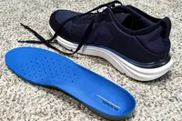 A Dr. Scholl's Men's Feel Ready Lace Up Sneaker with a separated insole placed on a textured floor