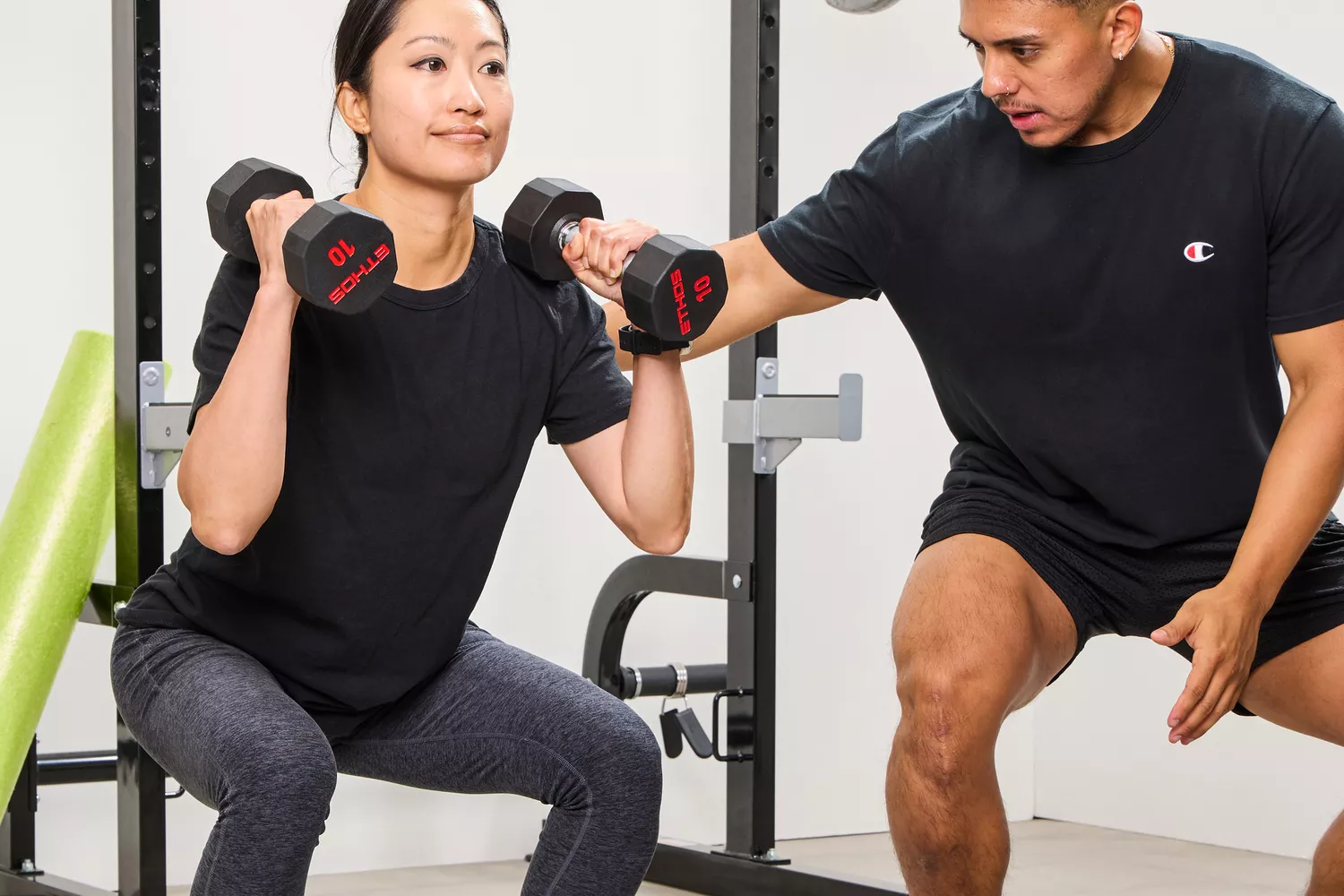 A person squats while lifting the ETHOS Rubber Hex Dumbbells