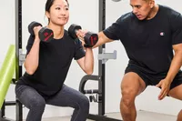 A person squats while lifting the ETHOS Rubber Hex Dumbbells