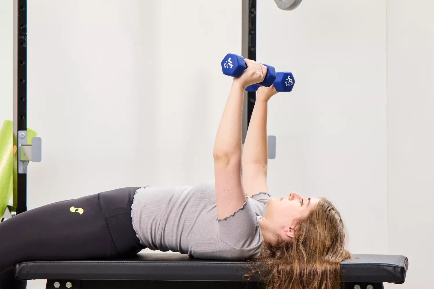A person does chest presses using the JFIT Dumbbell Set with Rack