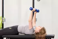 A person does chest presses using the JFIT Dumbbell Set with Rack