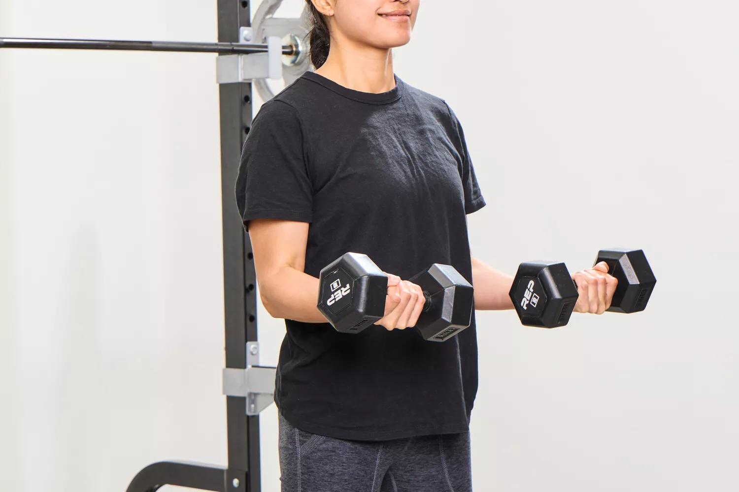 A person does arm curls using the REP Fitness Rubber Coated Dumbbells