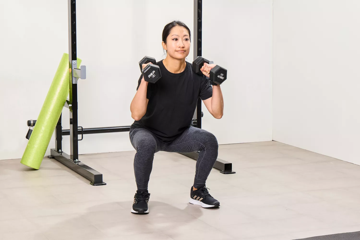 A person squats while holding the REP Fitness Rubber Coated Dumbbells