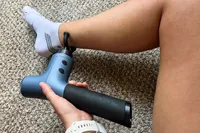 A person uses the Ekrin 365 Massage Gun on their ankle