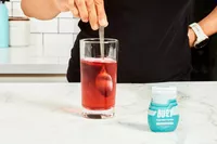 A person using a spoon to mix Buoy Electrolyte Drops with water