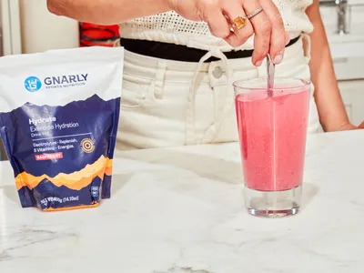 A person using a spoon to mix water with Gnarly Nutrition Hydrate Electrolyte Powder