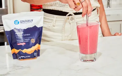 A person using a spoon to mix water with Gnarly Nutrition Hydrate Electrolyte Powder