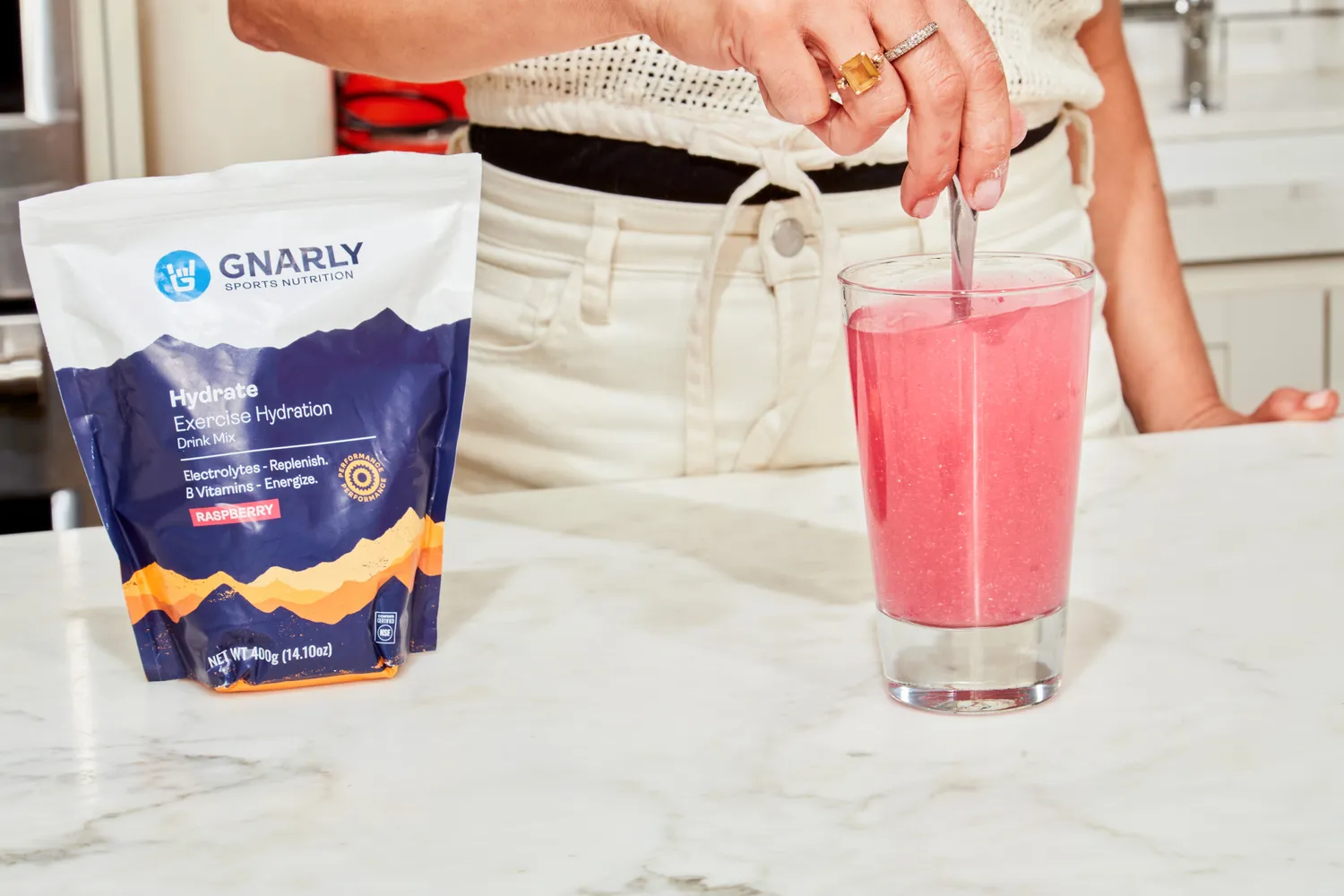 A person using a spoon to mix water with Gnarly Nutrition Hydrate Electrolyte Powder