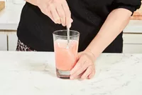A person using a spoon to mix water with Hydrant Hydrate Hydration Drink Mix inside a glass on a counter