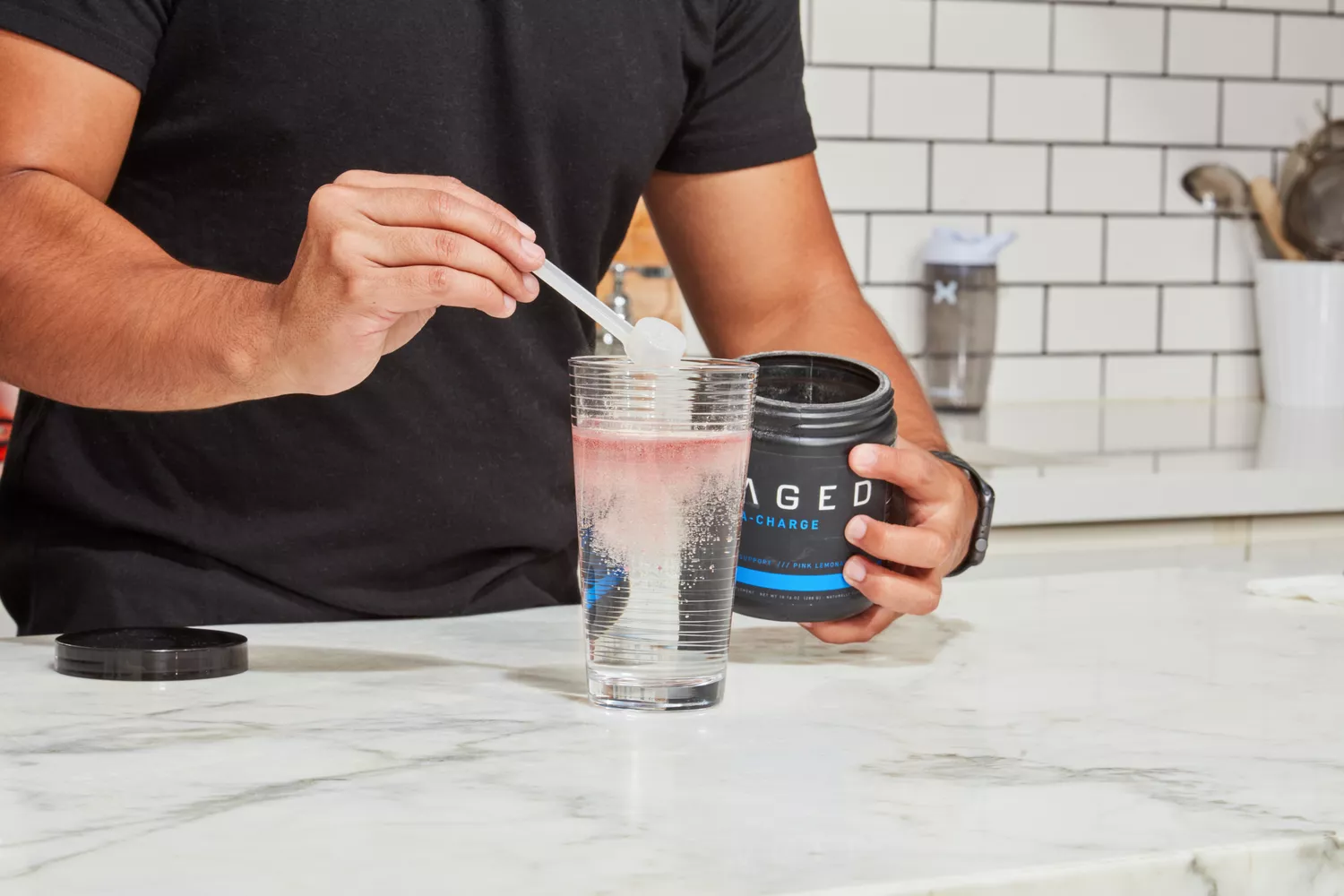 A person adding a scoop of Kaged Hydra Charge into a glass of water