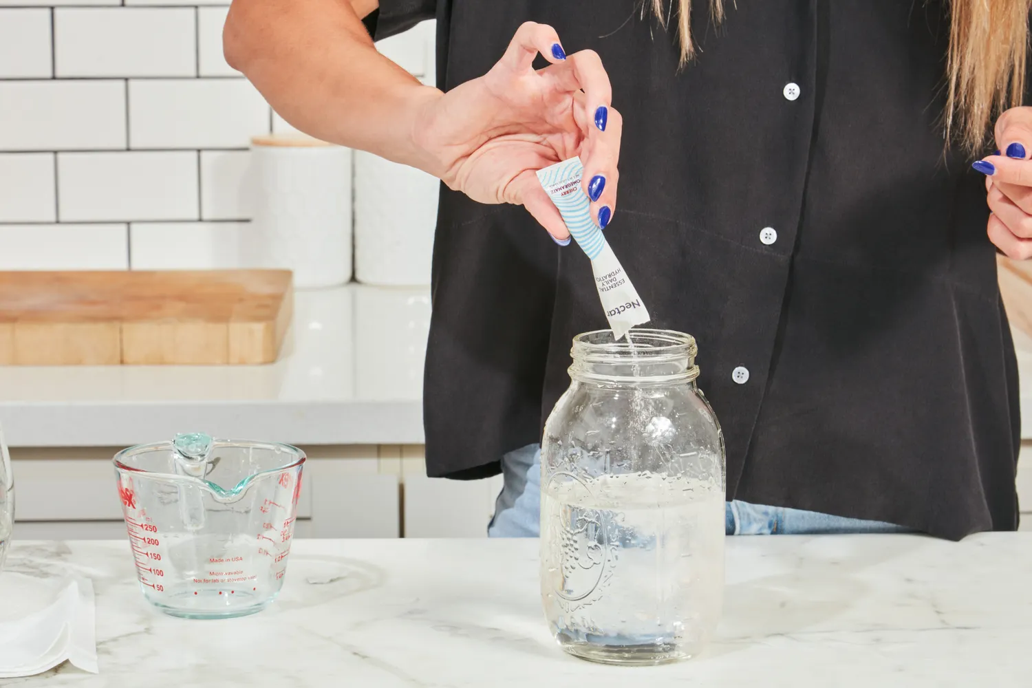 A person adding a packet of Nectar Daily Hydration into a mason jar filled with water