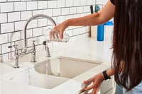 A person pouring a clear drink into the sink