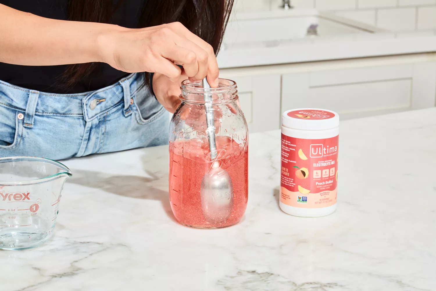 A person using a spoon to mix Ultima Replenisher Electrolyte Hydration Powder into water