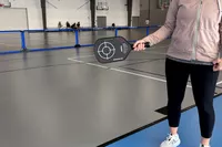 A person holding the Engage Pickleball Aero | Raw Toray T700 to the side on a n indoor court
