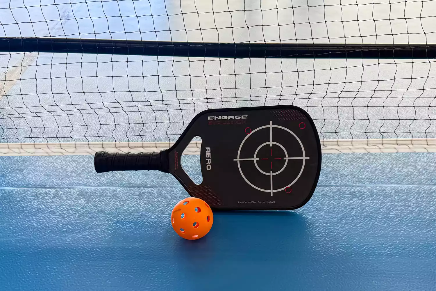 The Engage Pickleball Aero | Raw Toray T700 on a floor next to a net and ball