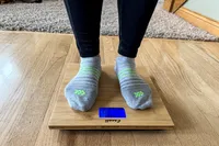 A front view of a person standing on the Escali Bamboo Digital Electronic Bathroom Scale in socks