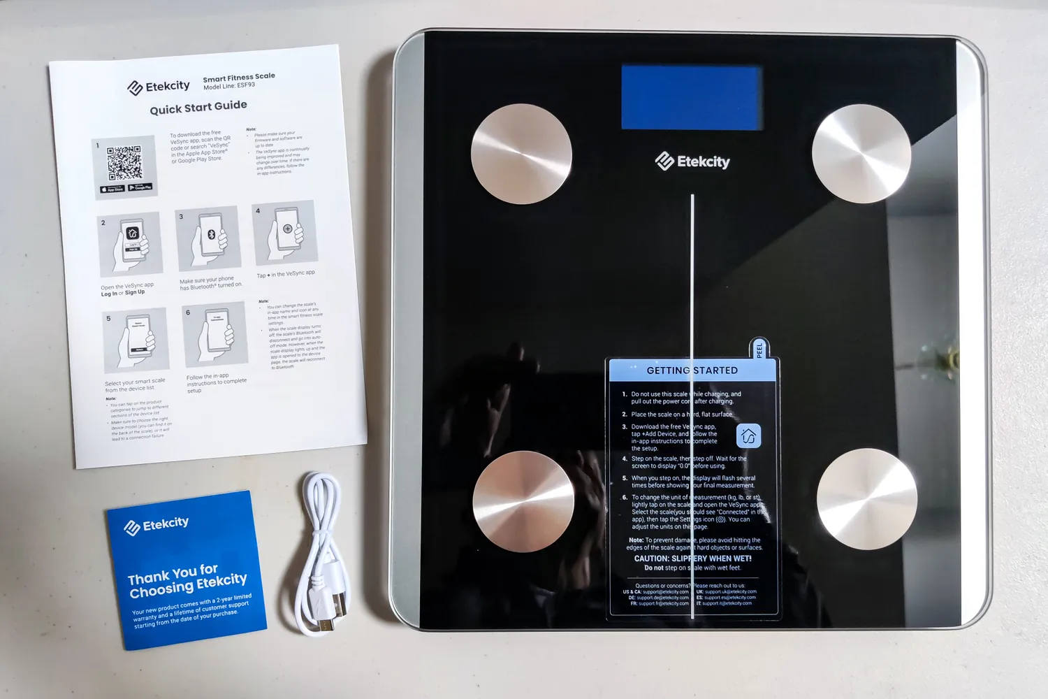 The Etekcity ESF93 Smart Fitness Scale next to the manual and charging cable