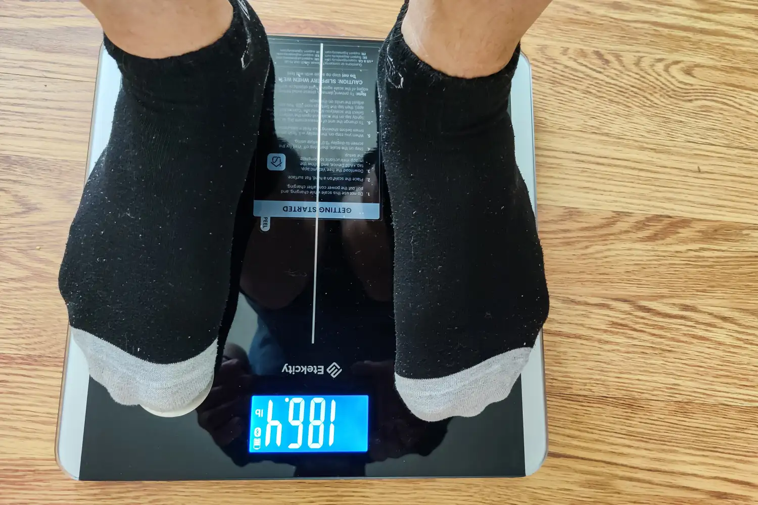 A person stands on the Etekcity ESF93 Smart Fitness Scale in socks