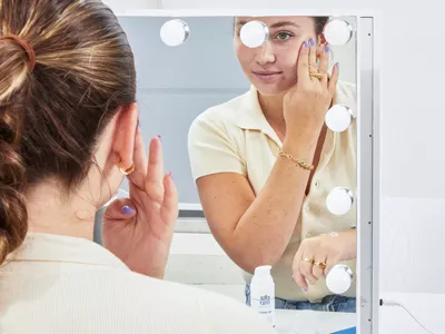 Person looking into a mirror applying EltaMD AM Therapy Face Moisturizer on their face